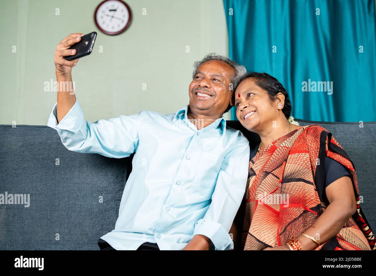 coppia anziana felice che prende selfie sul telefono mobile mentre si siede sul divano a casa - concetto di famiglia, di unione e di legame. Foto Stock