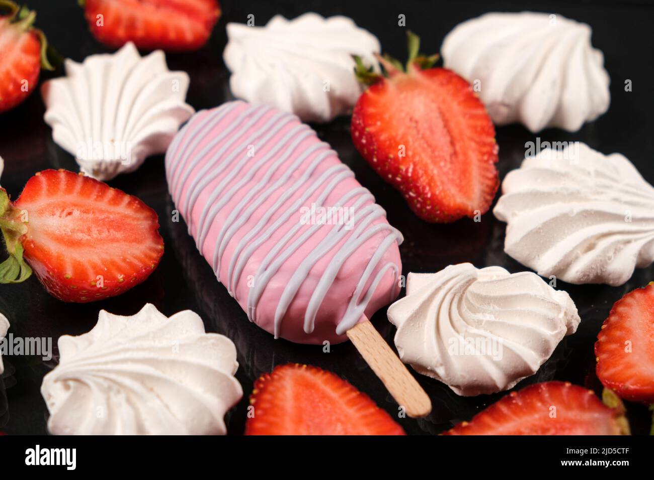 Gelato rosa su un bastone, meringa e fragole su sfondo nero. Foto Stock