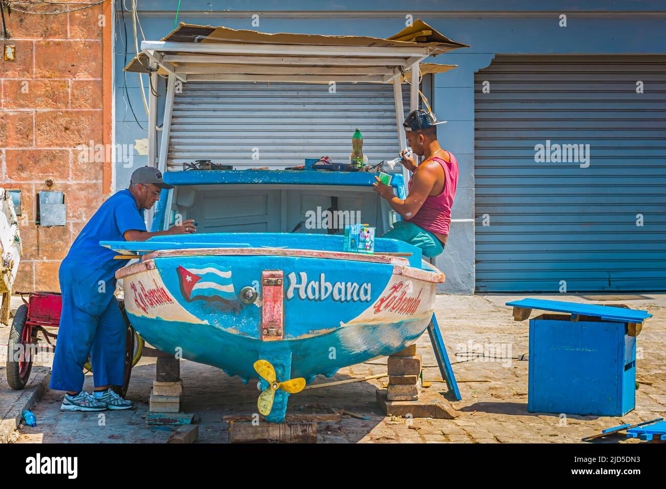 Due uomini dipingono una piccola barca blu per le strade di Old Havana, Cuba Foto Stock