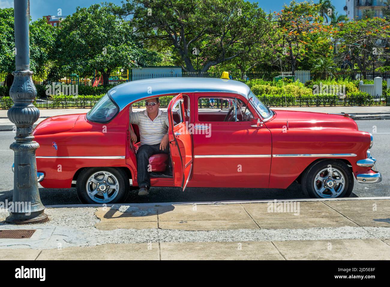 Il tassista si siede nel suo taxi rosso d'epoca e fa una pausa a l'Avana, Cuba Foto Stock