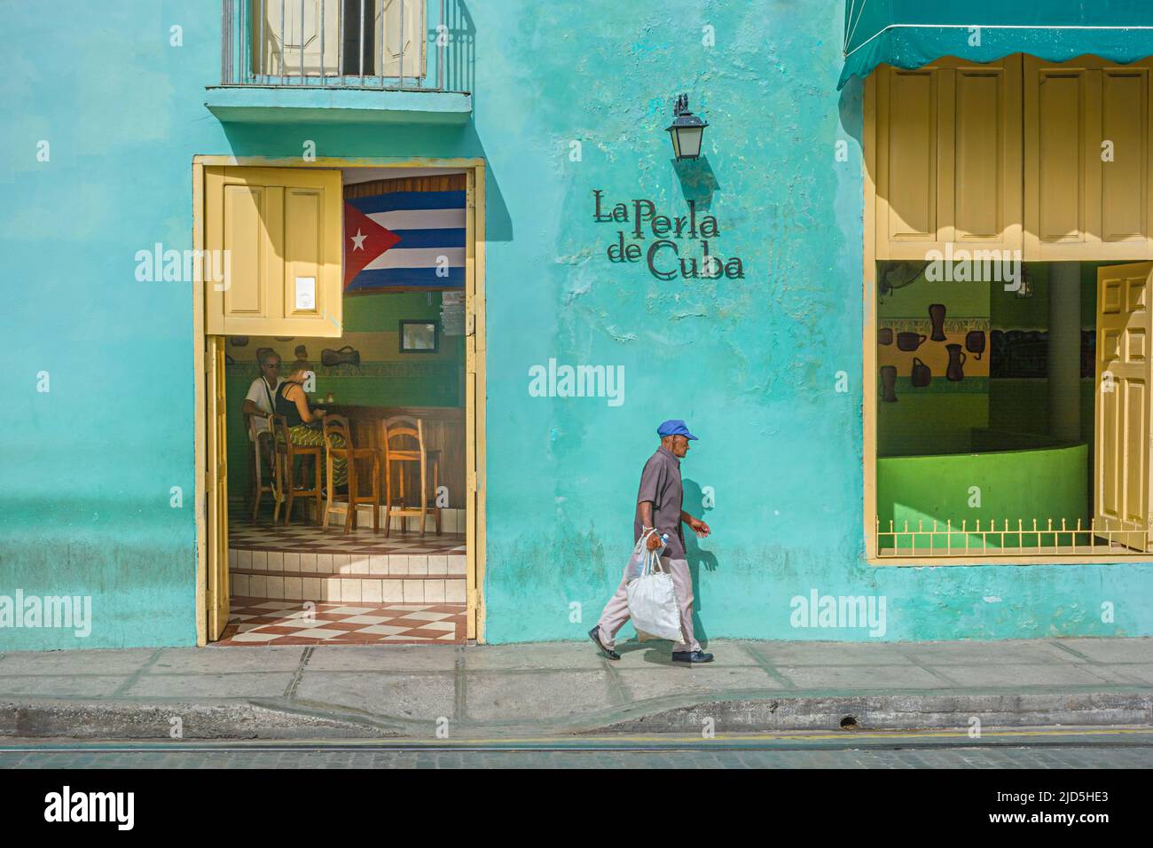 Un uomo cubano cammina davanti a un bar dipinto di verde chiaro a Camagüey, Cuba Foto Stock