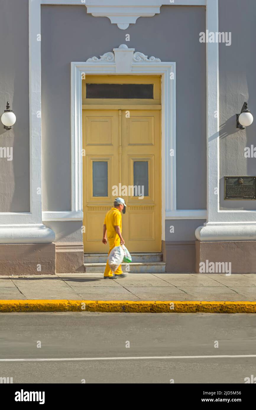 Un uomo più anziano in abiti gialli passa una bella porta gialla a Cienfuegos, Cuba Foto Stock