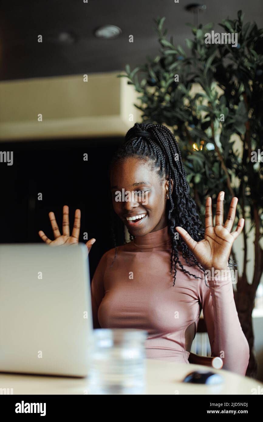 Gioiosa donna afroamericana emotivamente parlando gesturing su laptop online in caffetteria. Ragazza nera che lavora da remoto, freelance. Internet Foto Stock