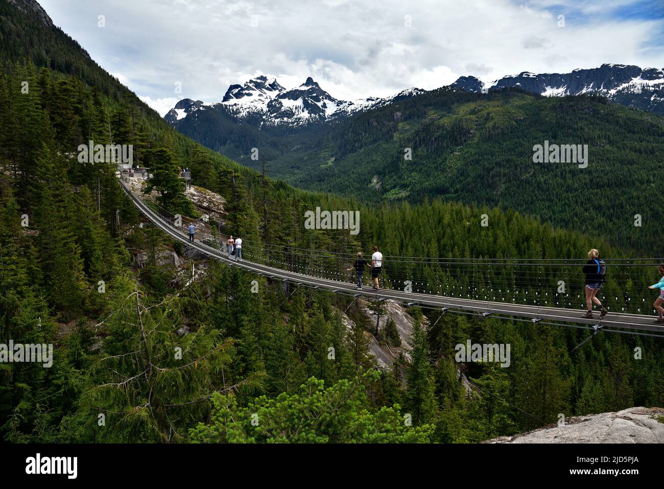 SQUAMISH, BC, CANADA, 02 GIUGNO 2019: Persone che attraversano un ponte sospeso con vista della montagna Sky Pilot innevata Foto Stock