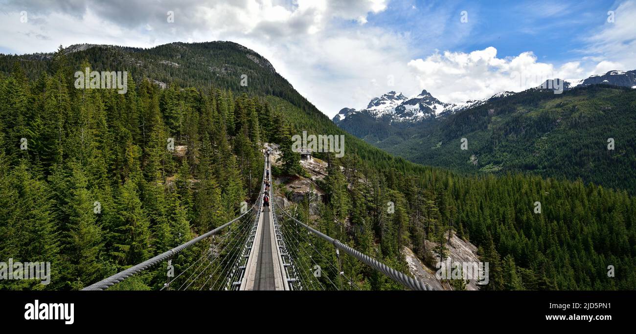 SQUAMISH, BC, CANADA, 02 GIUGNO 2019: Persone che attraversano un ponte sospeso con vista della montagna Sky Pilot innevata Foto Stock