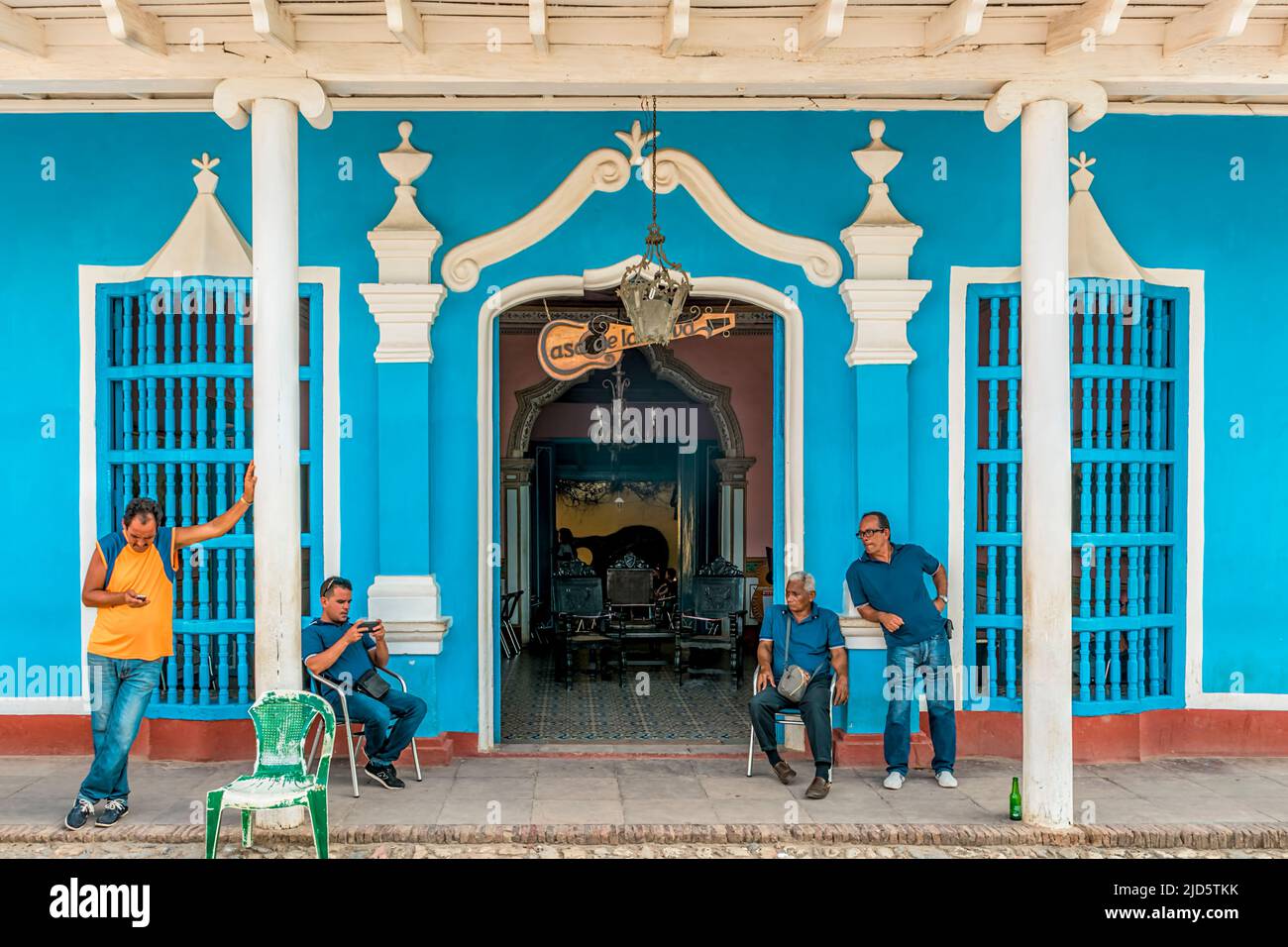 Quattro uomini seduti e in piedi fuori di un bel bar e controllare i loro telefoni a Trinidad, Cuba Foto Stock