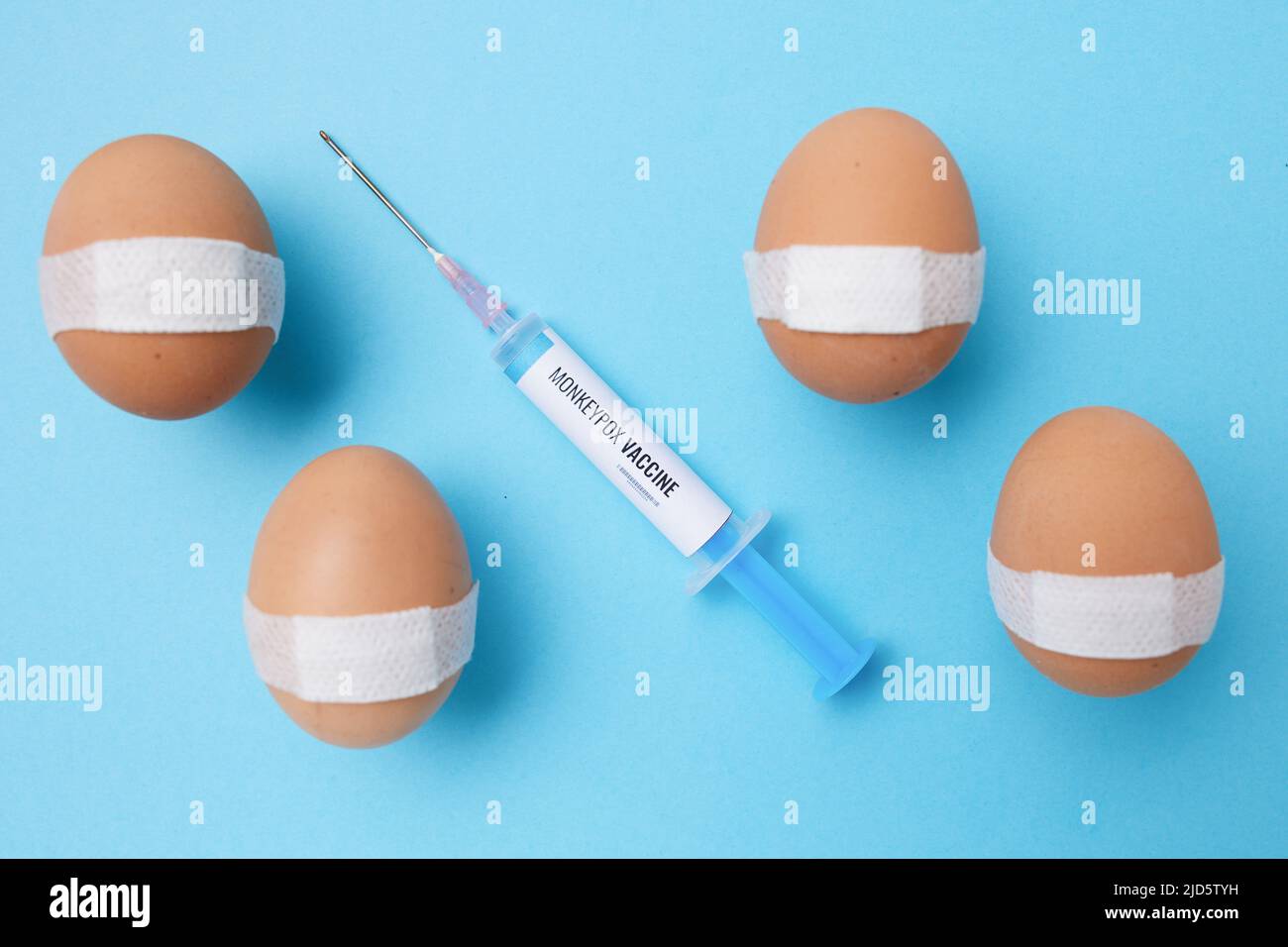 flatlay con siringa di vaccino di scimmietta e uova vaccinate con cerotto medico su sfondo blu. Foto Stock