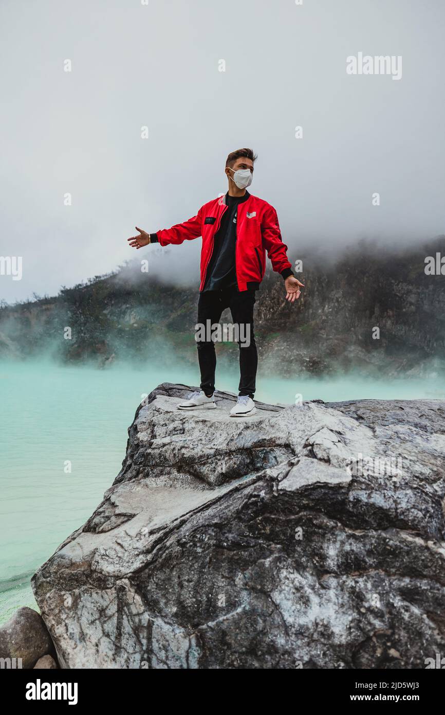 giovane uomo in bomber rosso in piedi sulla roccia al lago di kawah putih sulfer Foto Stock