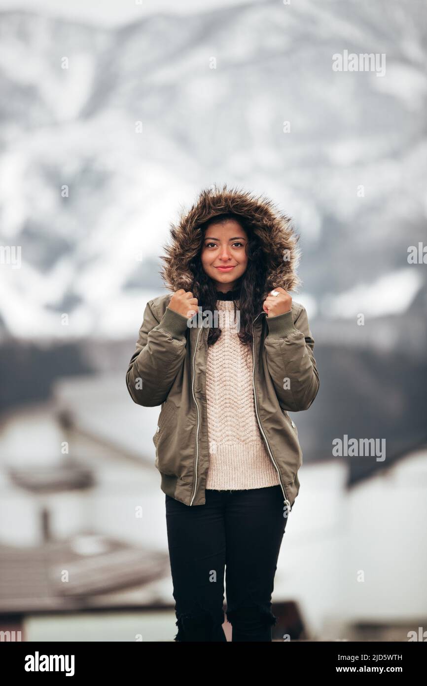 giovane ispanica donna in pelliccia verde giacca parka in inverno freddo con sfondo di montagna sfocato Foto Stock