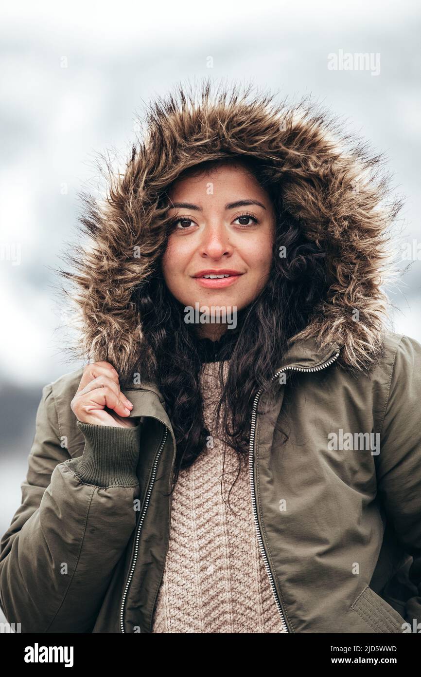 giovane ispanica donna in pelliccia verde giacca parka in inverno freddo con sfondo di montagna sfocato Foto Stock