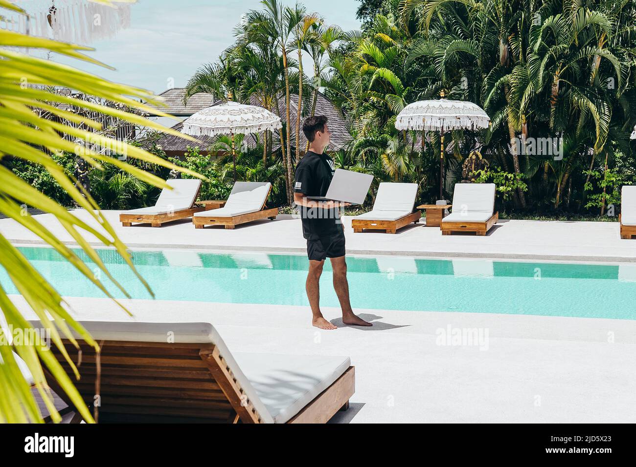 Giovane che lavora a Bali come nomade digitale vicino a pool su computer portatile Foto Stock
