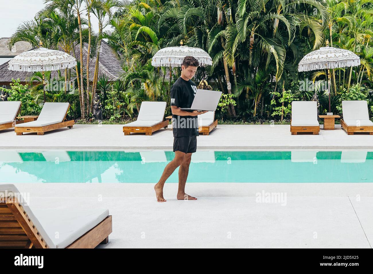 Giovane che lavora come nomade digitale con computer portatile vicino alla piscina di Bali Foto Stock
