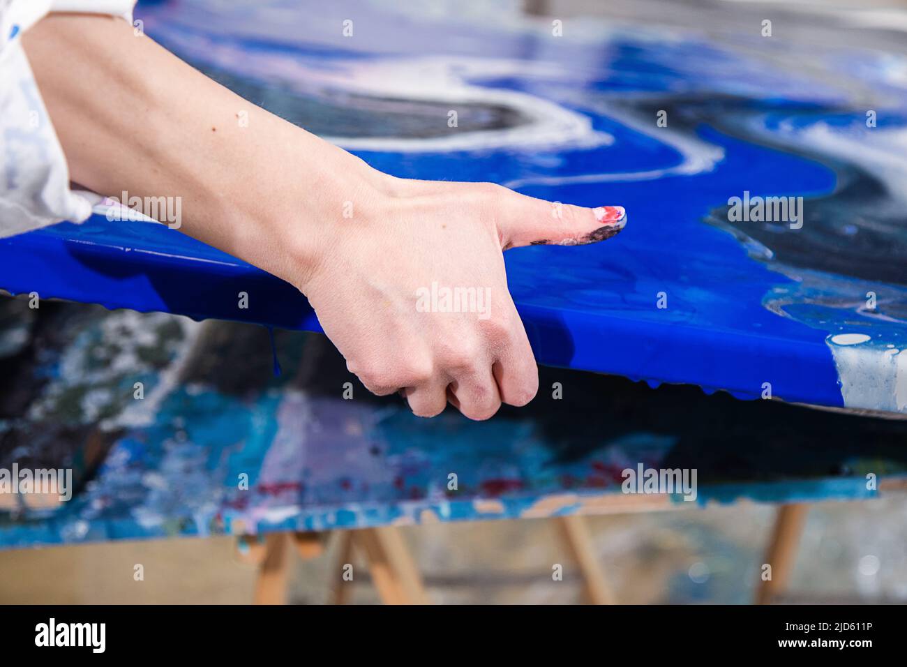 Foto ritagliata di mani di donna che reggono tela con un'immagine astratta di diversi colori blu, bianco, nero sulla scrivania. Foto Stock