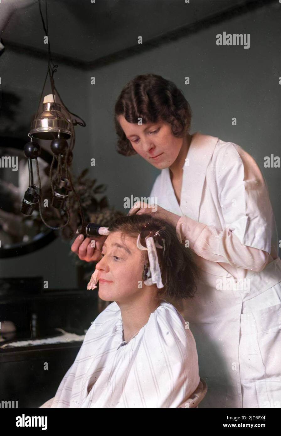 Un parrucchiere dà a una giovane donna un perm casa, utilizzando una macchina elettrica piuttosto pericolosa! Versione colorata di : 10168316 Data: Fine 1920s Foto Stock