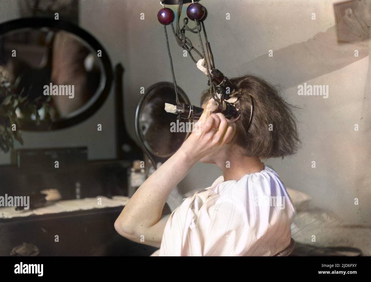 Una giovane donna si dà un perm di casa di fronte al suo tavolo da camera da letto, utilizzando un po 'pericoloso guardare apparato elettrico - speriamo che sia messo a terra! Versione colorata di : 10168321 Data: Fine 1920s Foto Stock