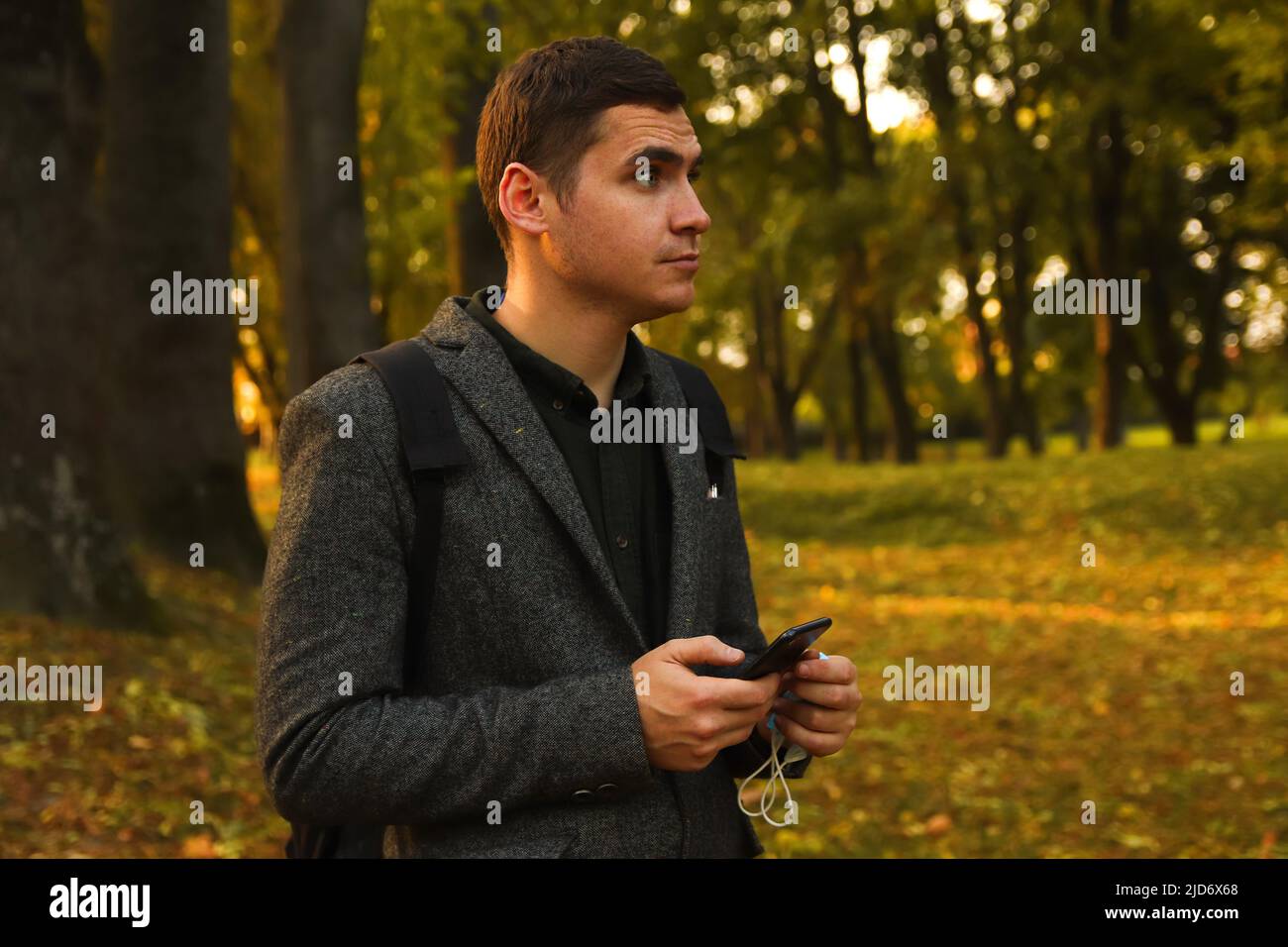 Defocalizzare il giovane uomo che tiene il telefono. Uomo che usa lo smartphone nel parco autunnale. Digitare un messaggio di testo o leggere i social media sul telefono cellulare. Sfondo autunno Foto Stock