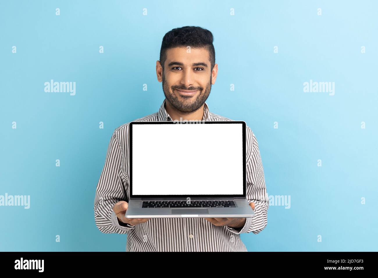 Guarda la pubblicità su Internet. Ritratto di allegro business con notebook con schermo vuoto, spazio per la copia di immagini o testo, indossando una maglietta a righe. Studio interno girato isolato su sfondo blu. Foto Stock