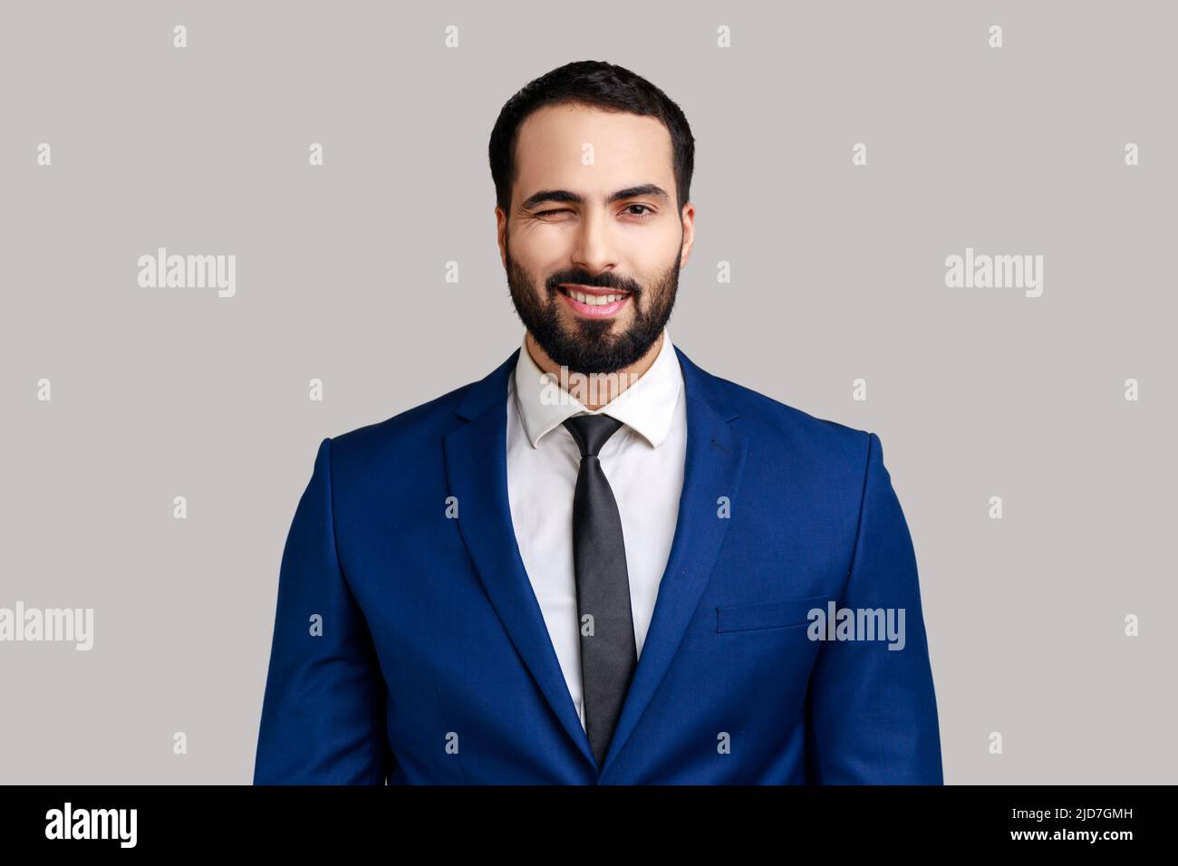 Ritratto di uomo d'affari barbuto di buon umore, sorridendo ampiamente e sverrando alla macchina fotografica con il sorriso toothy, indossando il vestito ufficiale di stile. Studio interno girato isolato su sfondo grigio. Foto Stock