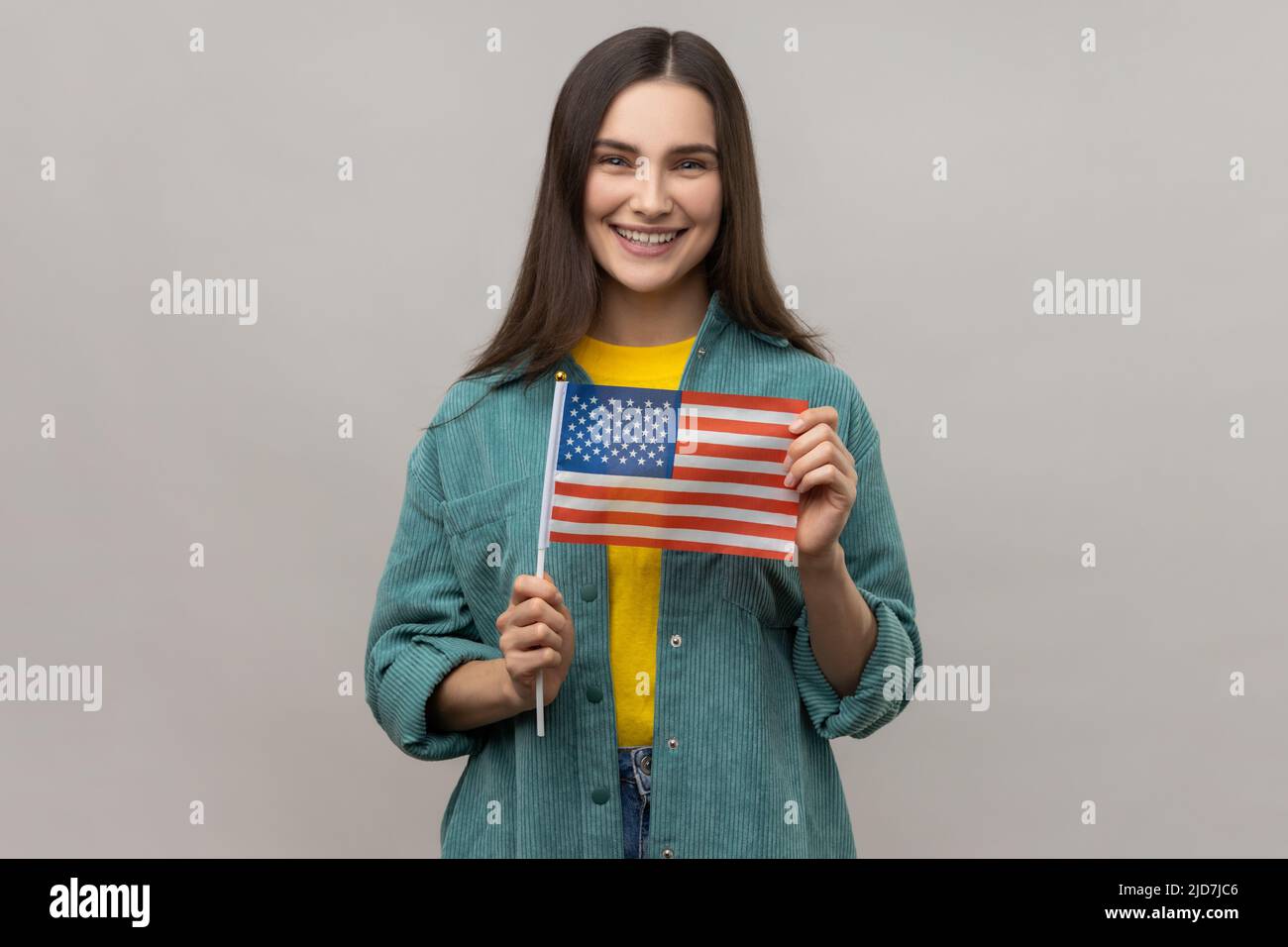 Ritratto di giovane donna felice soddisfatto in piedi e tenendo bandiera americana, festeggiamenti nazionali, indossando giacca casual stile. Studio interno girato isolato su sfondo grigio. Foto Stock