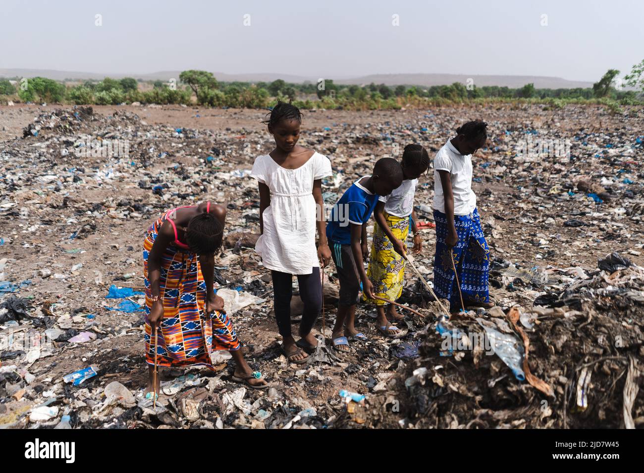 Un gruppo di bambini che frugano attraverso un campo coperto di rifiuti per trovare materiale riciclabile da vendere, un simbolo di estrema povertà nelle aree subsahariane Foto Stock