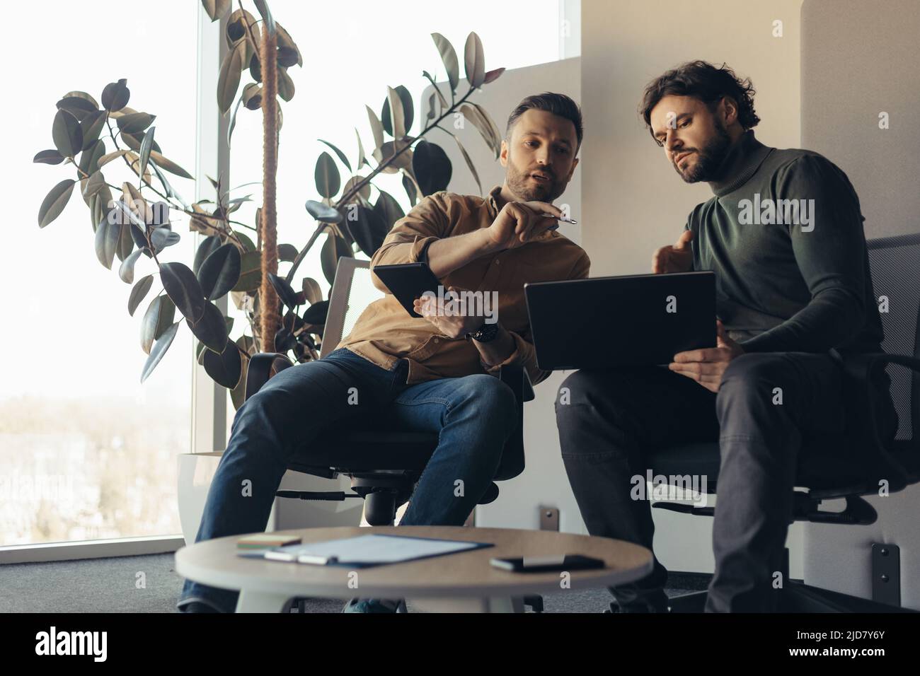 Colleghi di sesso maschile che parlano di progetti aziendali, brainstorming per idee, uso di computer portatili in uffici moderni Foto Stock