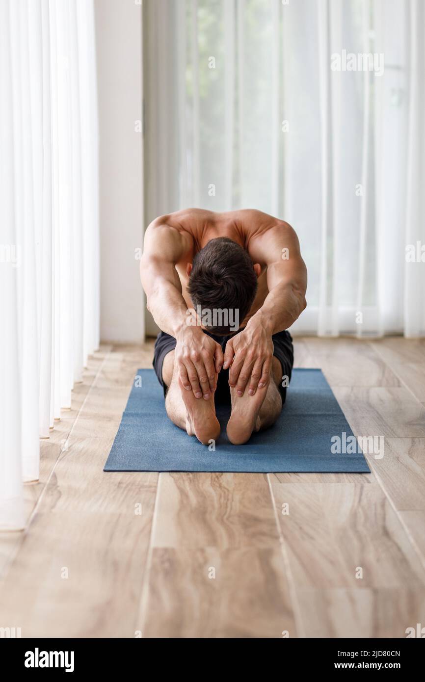 Giovane uomo yoga che fa le gambe stretching durante la routine del mattino Foto Stock