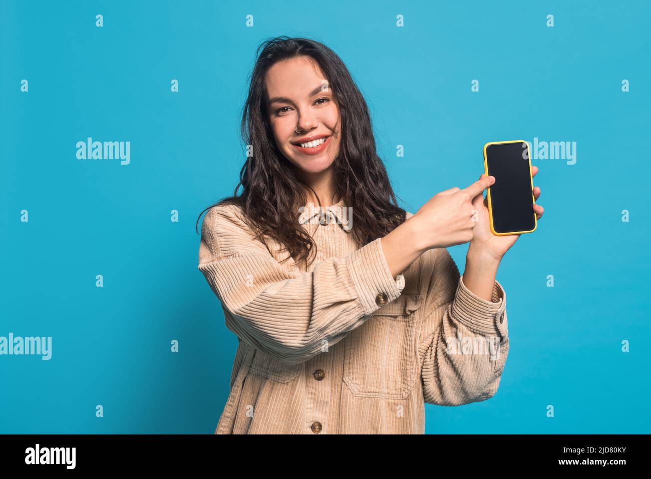 Sorridente felice millenario donna caucasica brunette studente blogger in casuale puntino dito su smartphone con schermo vuoto Foto Stock