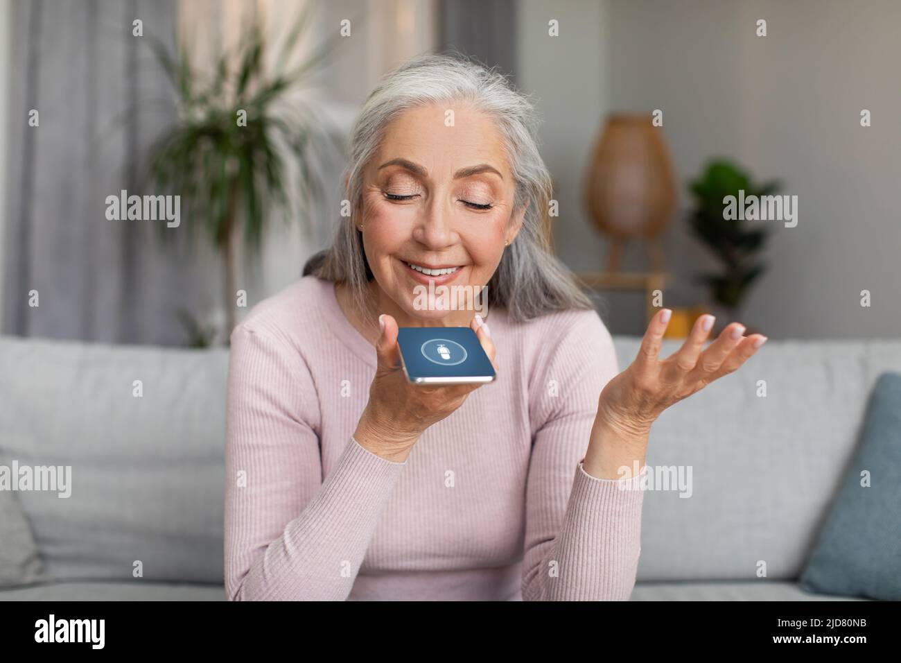 Allegro maturo europeo grigio-capelli donna parla da smartphone hanno chiamata da solo in soggiorno interno Foto Stock