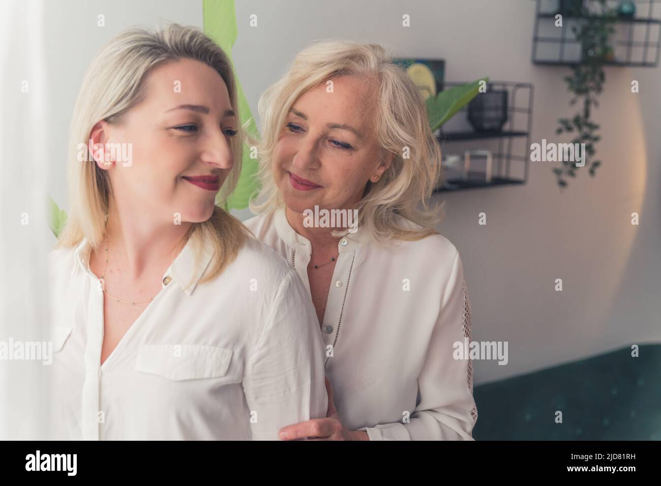 Due donne europee con capelli biondi e camicie bianche con bottoni che si accamonano l'una accanto all'altra in un moderno soggiorno. Foto di alta qualità Foto Stock