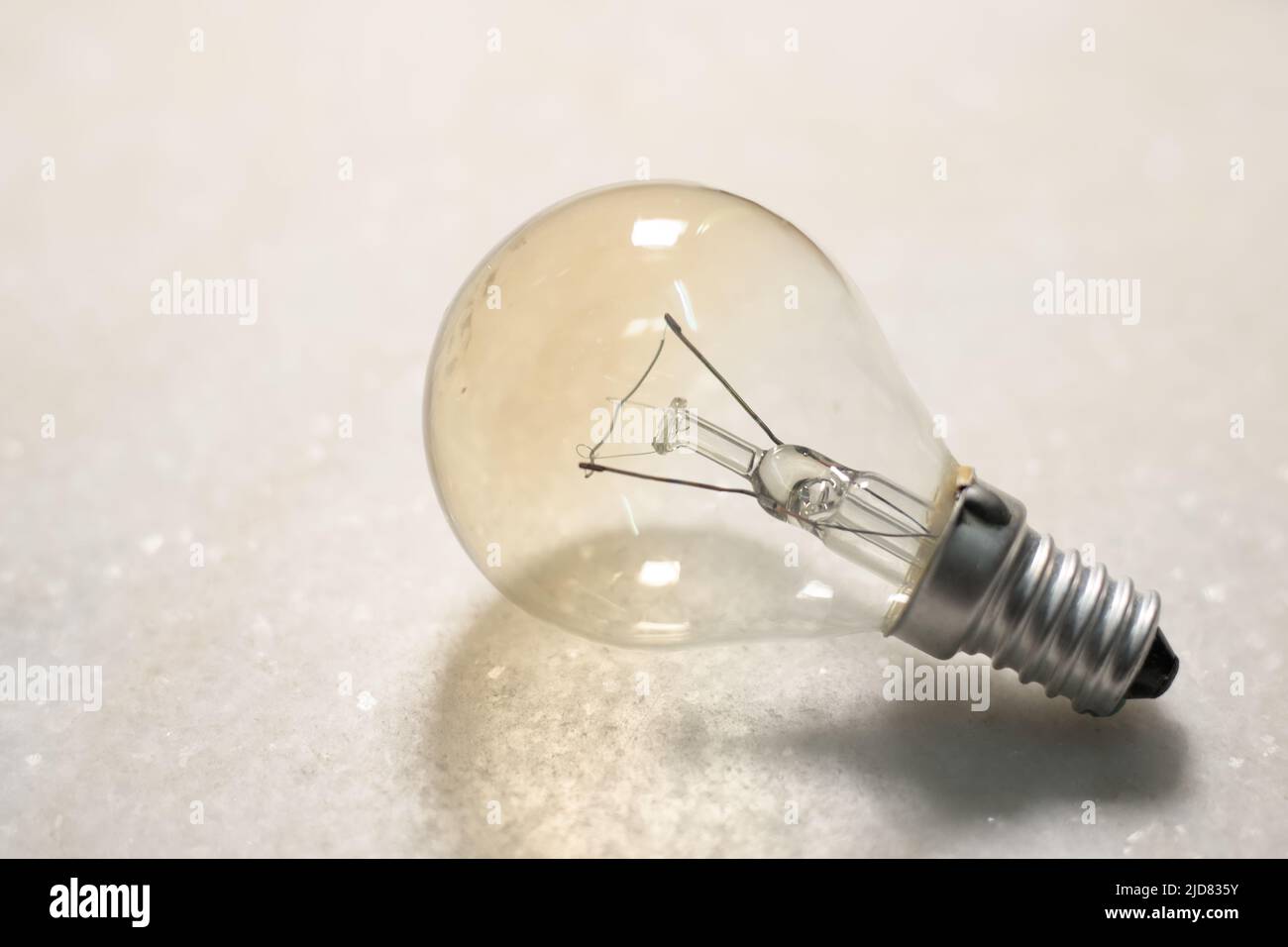 Una piccola lampadina a incandescenza o una lampada su una superficie rigida bianca Foto Stock