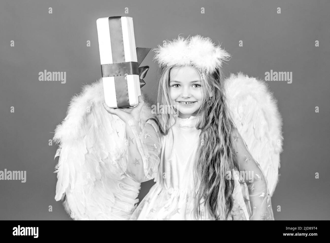 San Valentino. Felice sorridente ragazza cupid. Angelo capretto con regalo. Piccolo angelo con ali bianche contiene il regalo. Ragazza angelica giocosa. Carino angelo bambino Foto Stock