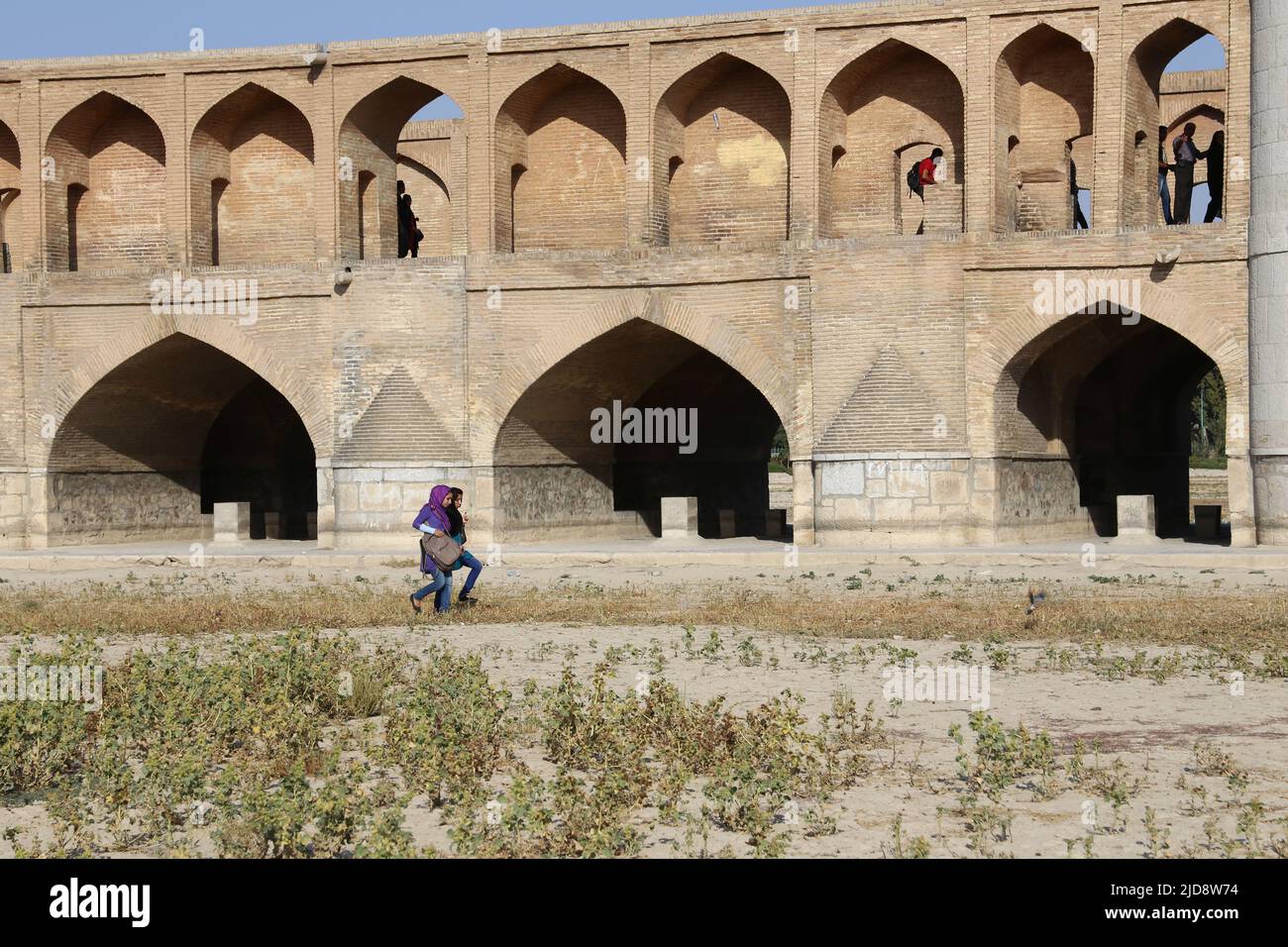 Allah-Verdi-Khan-Brücke a Isfahan, Iran. Auf persisch heißt sie si-o-se Pol. Die Brücke hat zwei Etagen und überspannt den Zayandeh Rud. Die Brücke Hat 33 Bögen. Der si-o-se Pol ist meistens ausgetrocknet. Blick von der Flussseite auf die Brücke. Zwei Frauen queren den Fluss neben der Brücke. Foto Stock