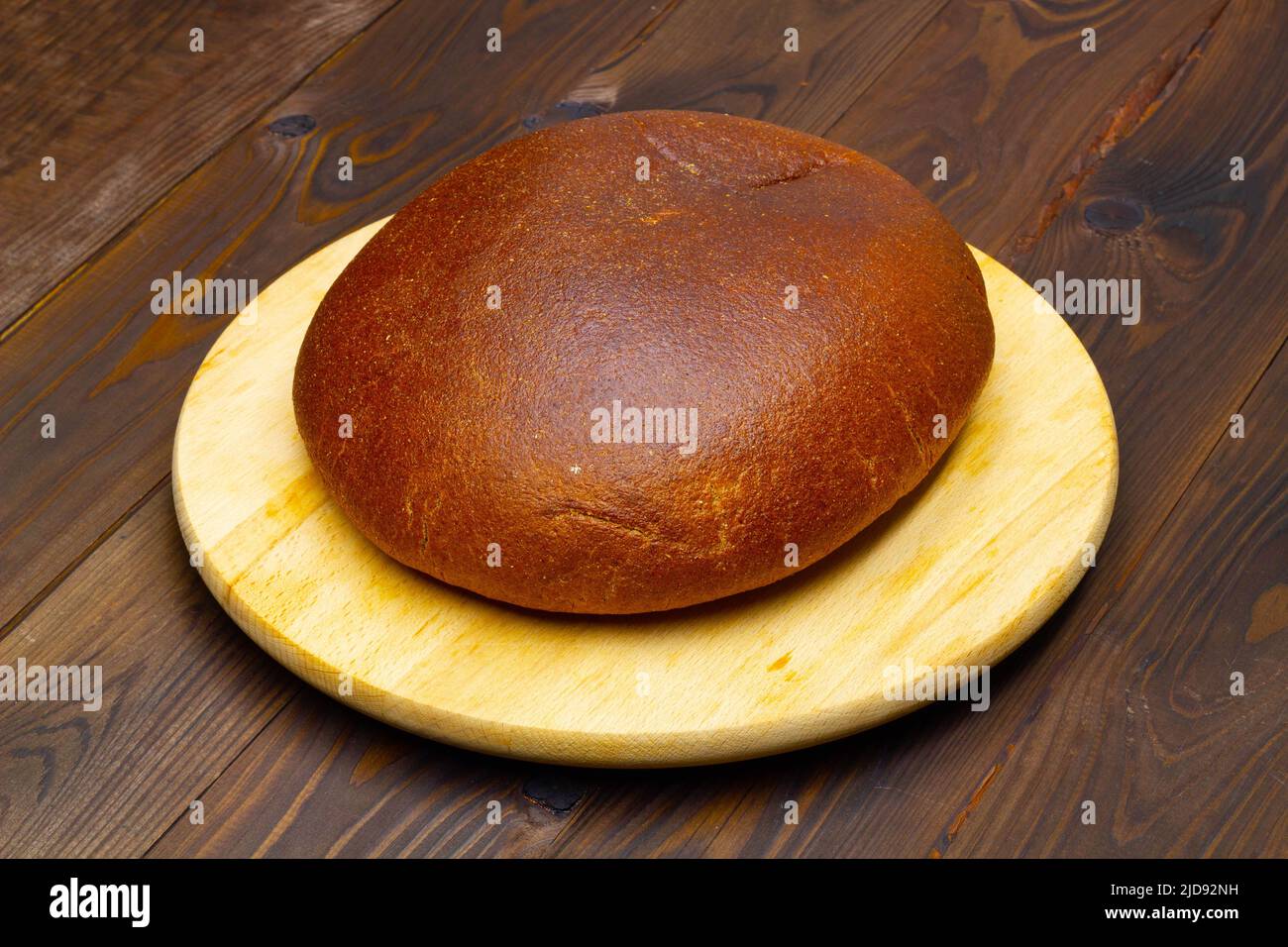 Una pagnotta di pane nero. Pane fatto in casa nel forno in un pezzo unico. Pane rotondo ecologico su un tagliere bianco, contro un bel marrone Foto Stock