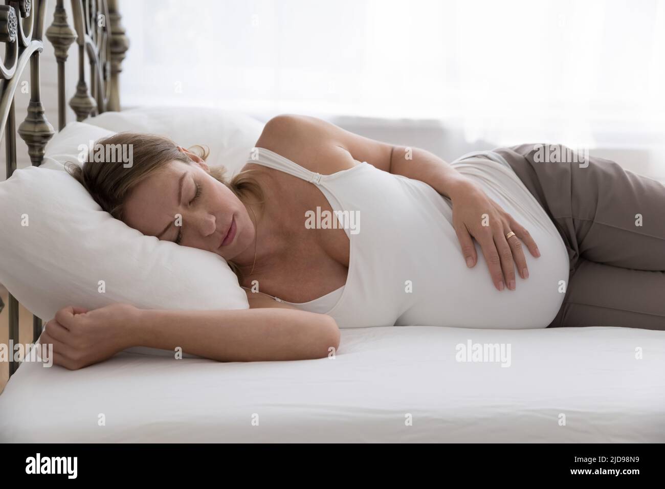 La donna incinta dorme a letto cercando esausta a causa di una gravidanza dura Foto Stock