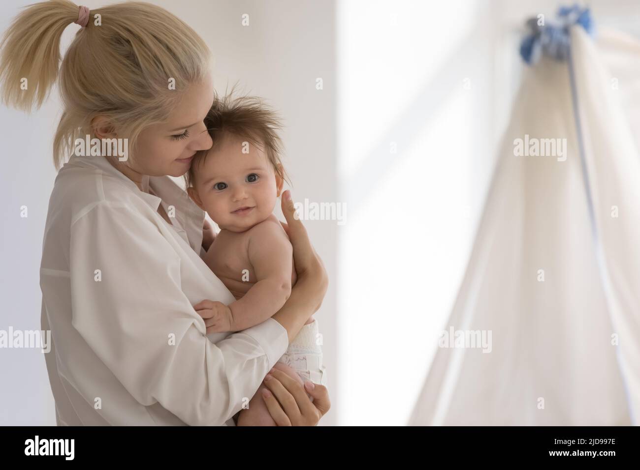 Giovane madre in piedi in cuccioli di stanza dei bambini, lulls il suo bambino adorabile Foto Stock