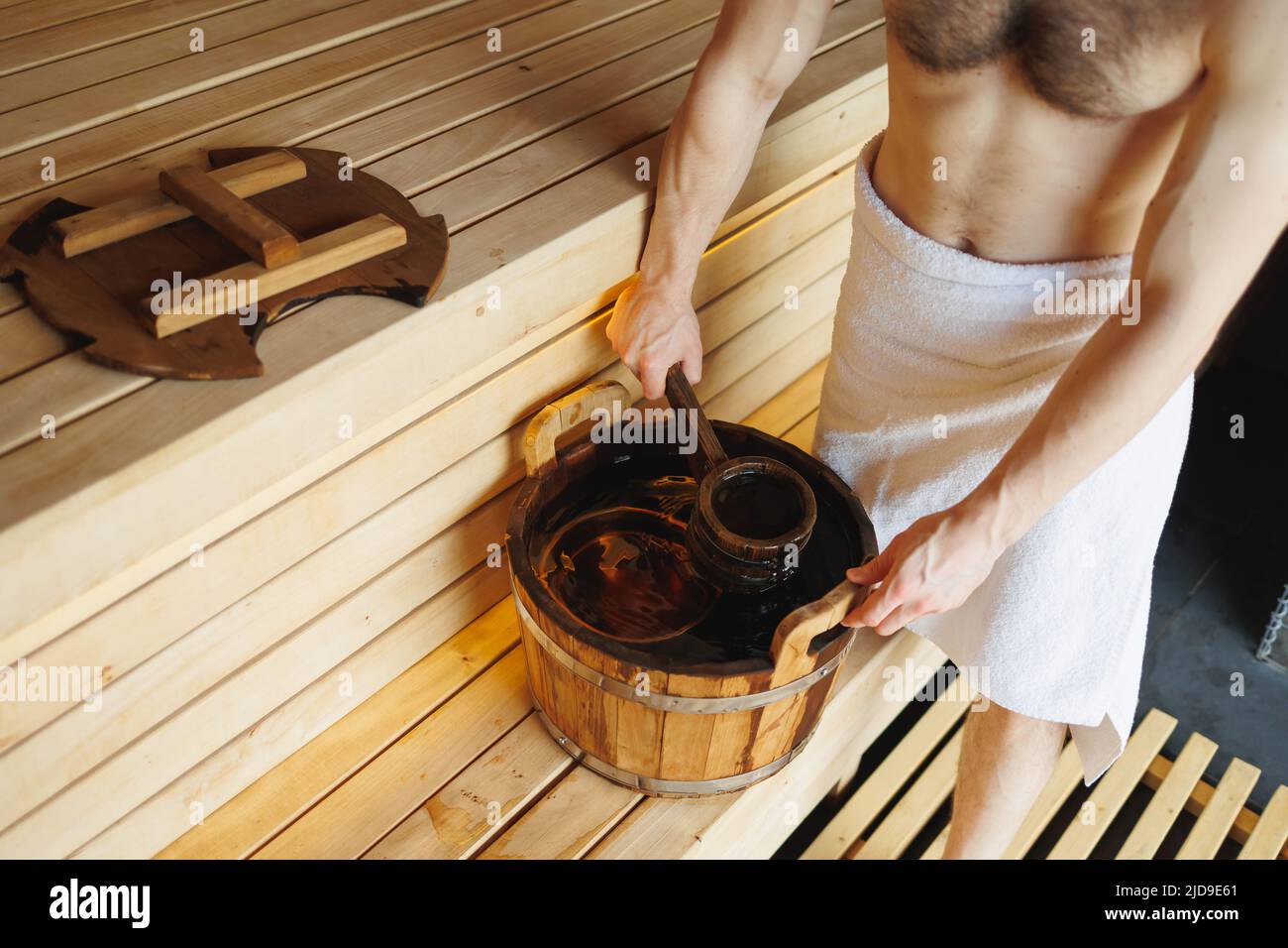 Uomo che raccoglie acqua da secchio di legno in sauna. Il centro benessere è disponibile nel bagno turco Foto Stock