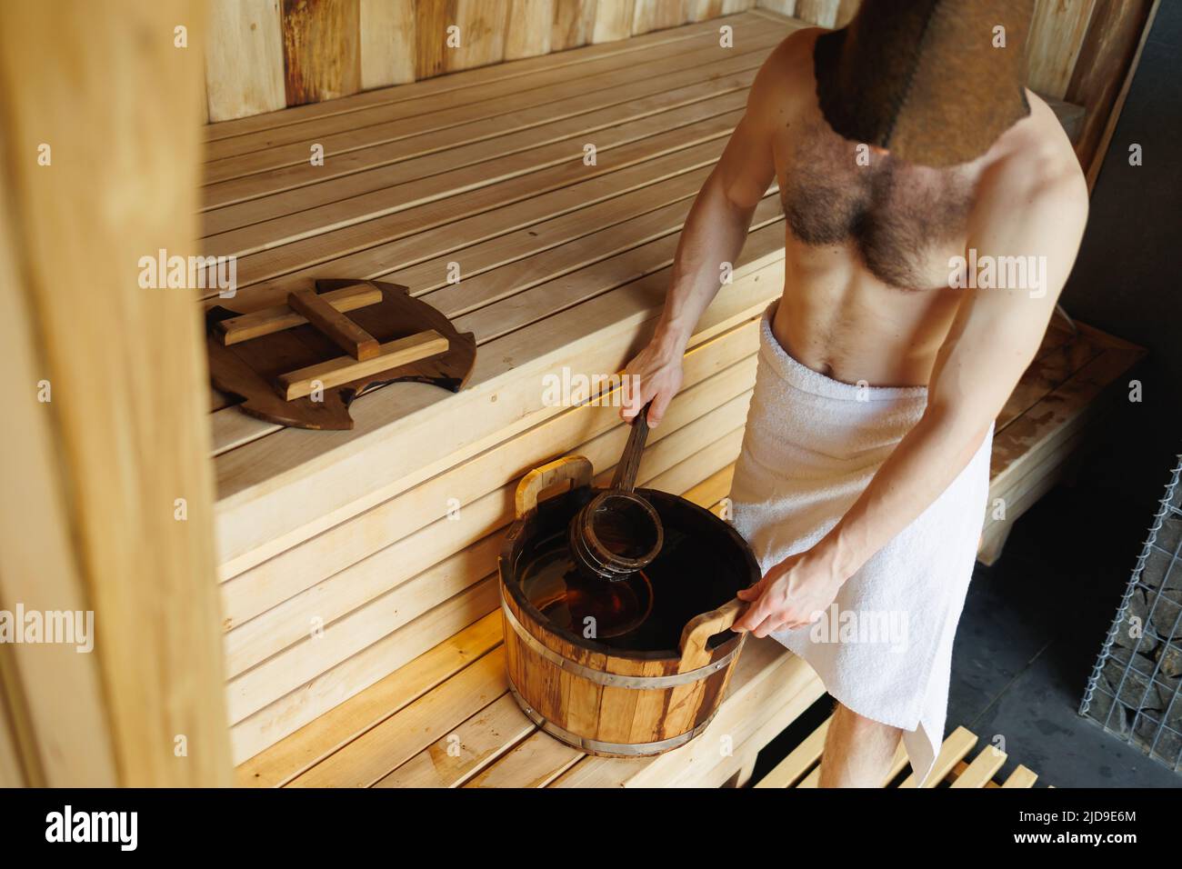 Uomo che raccoglie acqua da secchio di legno in sauna. Uomo che riposa in un bagno di vapore Foto Stock