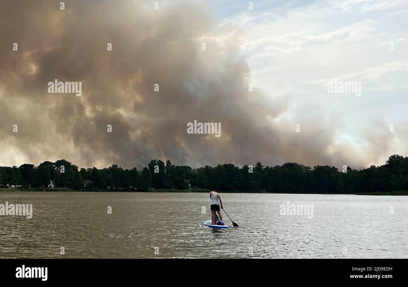 Seddin, Germania. 19th giugno 2022. Un giovane uomo si erge su un SUP sul lago Seddin, mentre una nuvola di fumo dal fuoco della foresta vicino Treuenbrietzen è visibile per chilometri. Vigili del fuoco ci sono stati combattimenti un fuoco di foresta per giorni. I venti crescenti hanno aggravato la situazione la domenica al fuoco della foresta, che è scoppiato il 17.06.2022. Credit: Stephanie Pilick/dpa/Alamy Live News Foto Stock