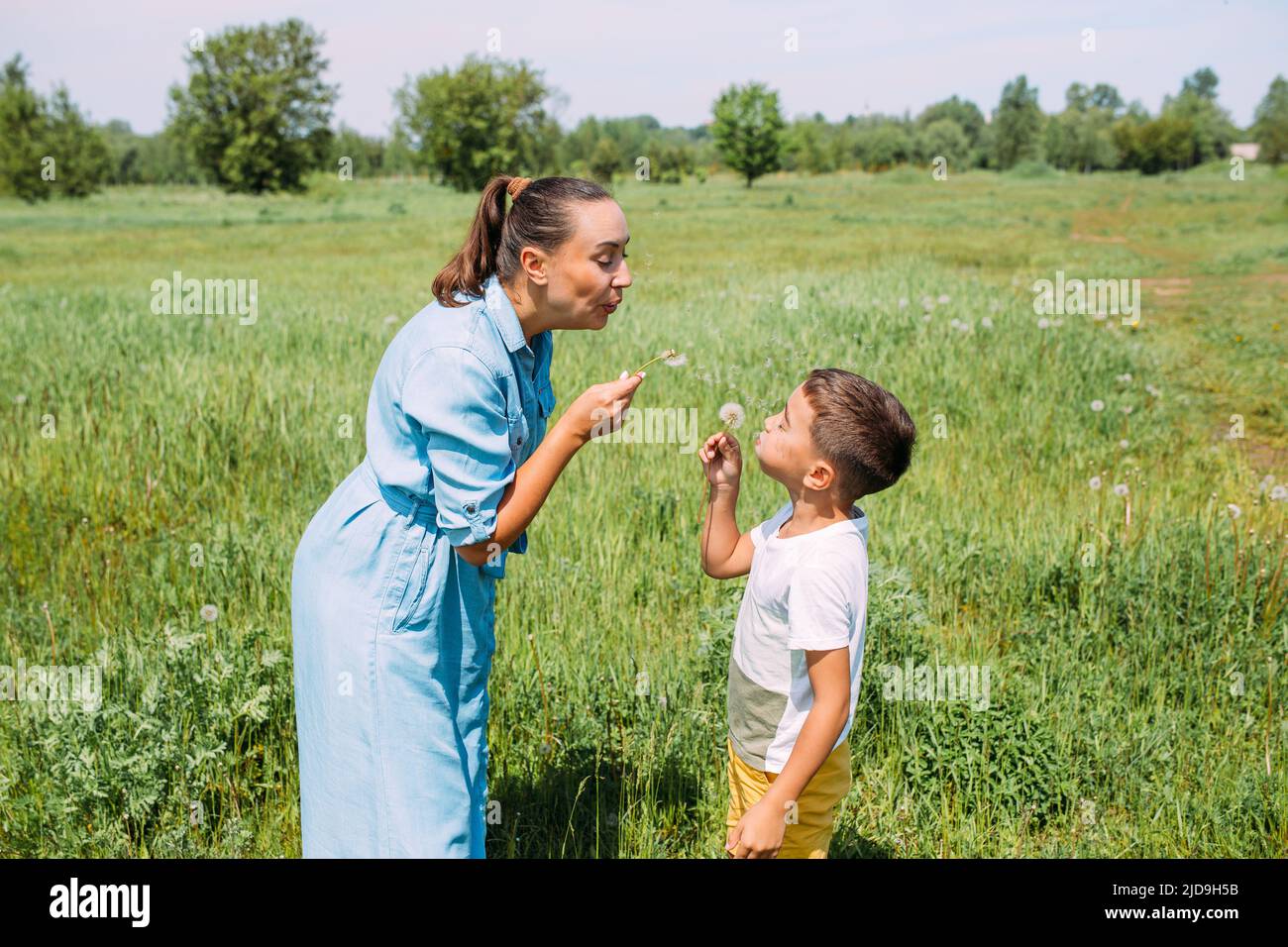 I preschoolers del figlio e della mamma trascorrono il tempo all'aperto in estate e soffiano sui dandelions Foto Stock