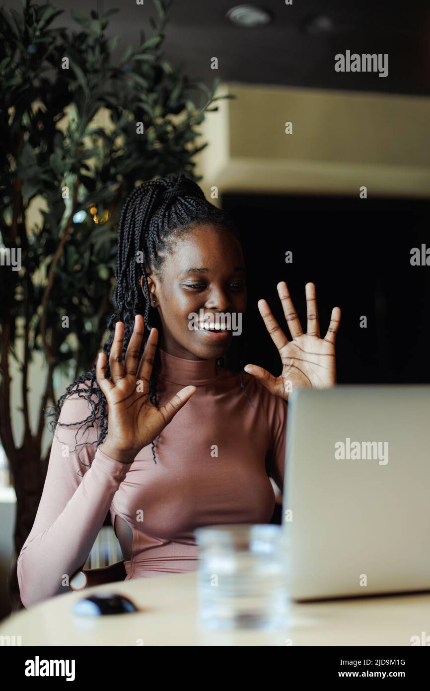 Gioiosa donna afroamericana emotivamente parlando gesturing su laptop online in caffetteria. Ragazza nera che lavora da remoto, freelance. Internet Foto Stock