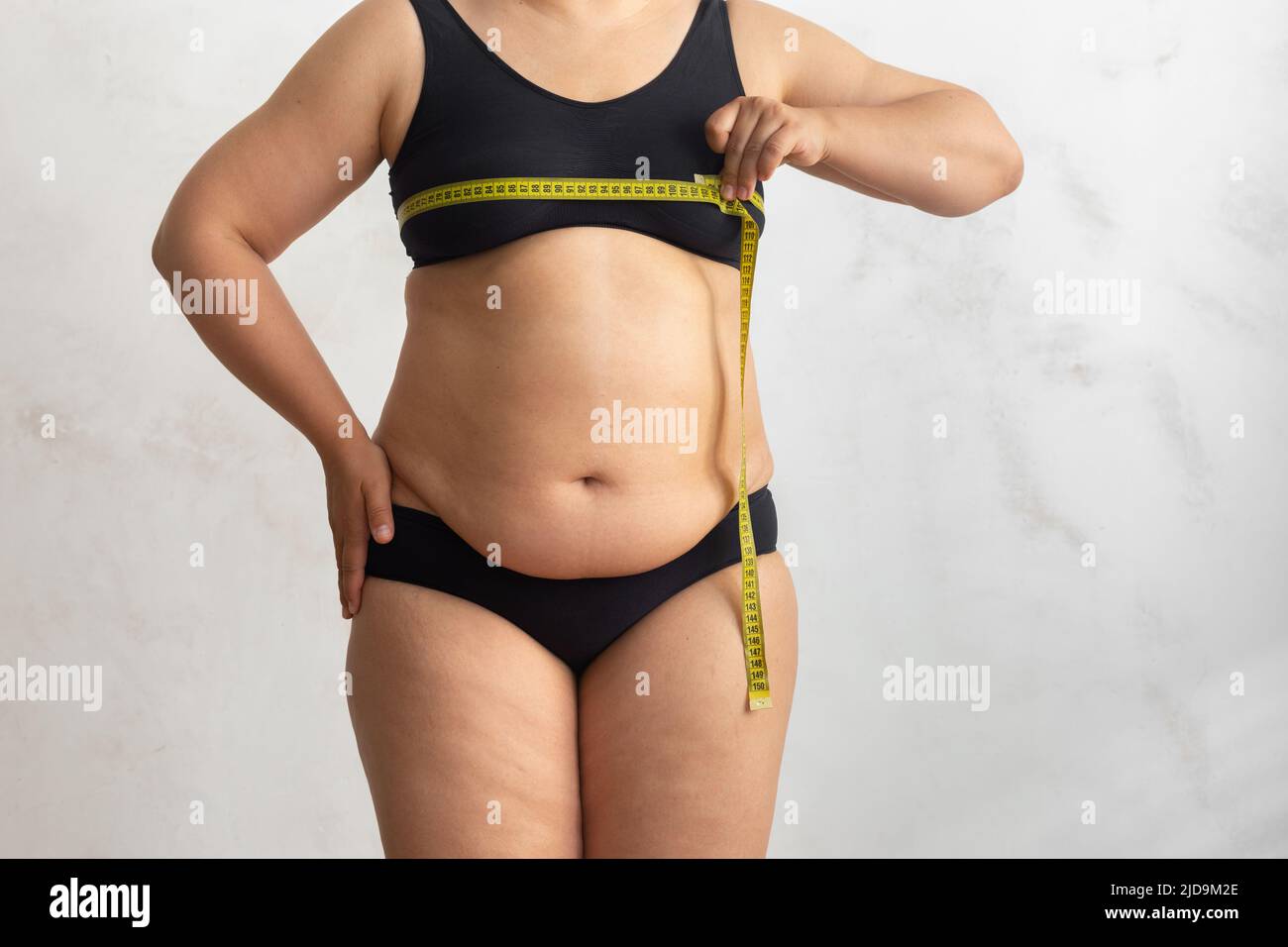 Croppata sovrappeso, grasso, donna adiposa in lingerie nero, misurare petto da roulette nastro. Dimagrimento, perdita di peso, dieta Foto Stock