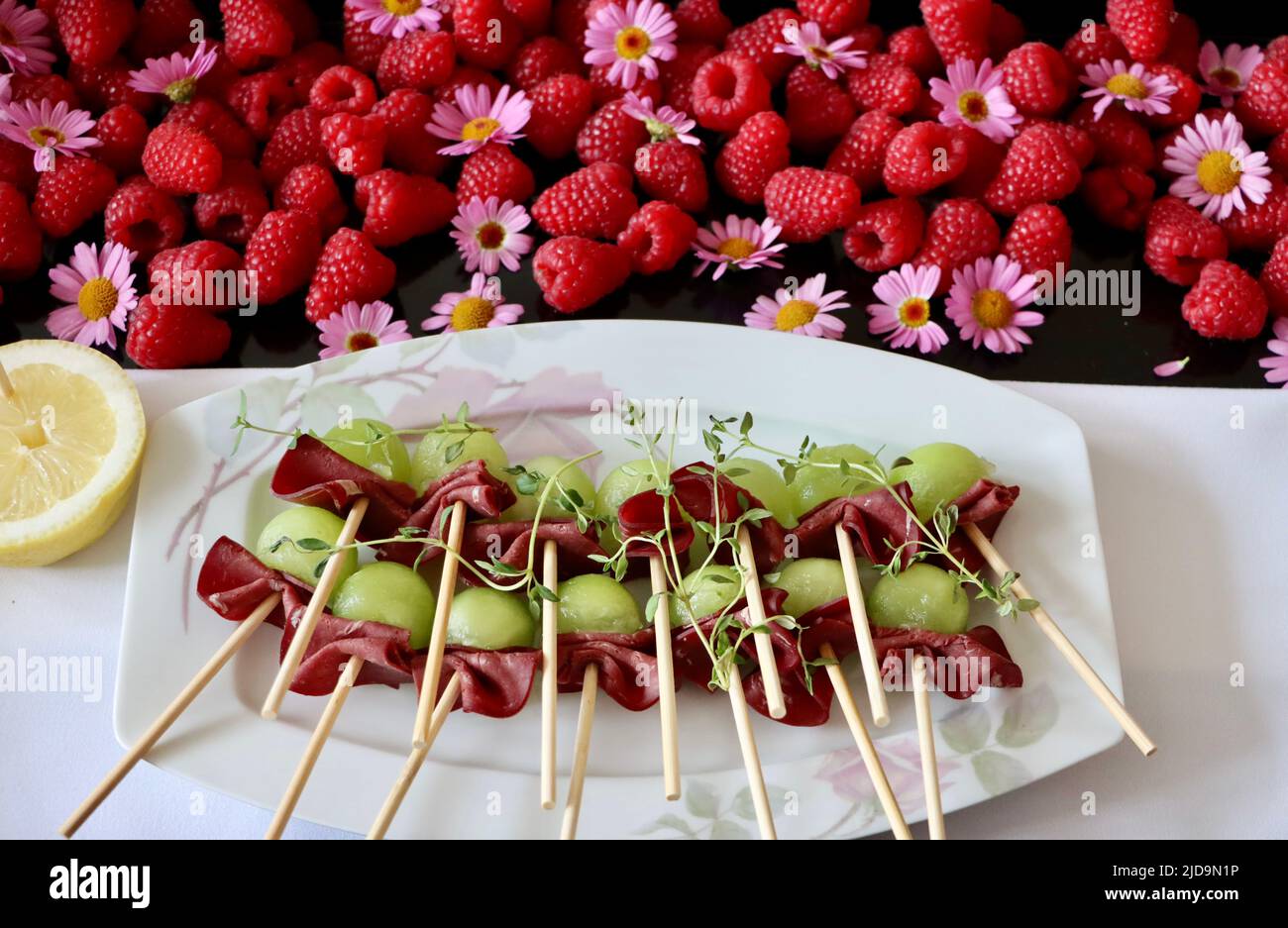 Spiedini di bambù con renna affumicata e melone su vassoio decorato con lamponi e fiori viola. Foto Stock