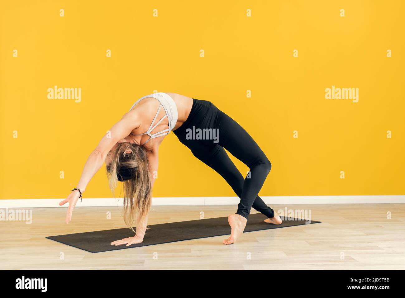 Giovane donna attraente che pratica yoga, in piedi in un esercizio, indossando abbigliamento sportivo bianco e nero, sfondo giallo studio, vista laterale Foto Stock