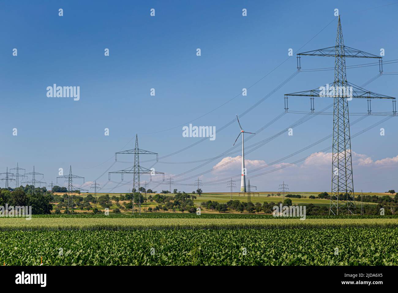una turbina eolica si trova tra piloni ad alta tensione Foto Stock