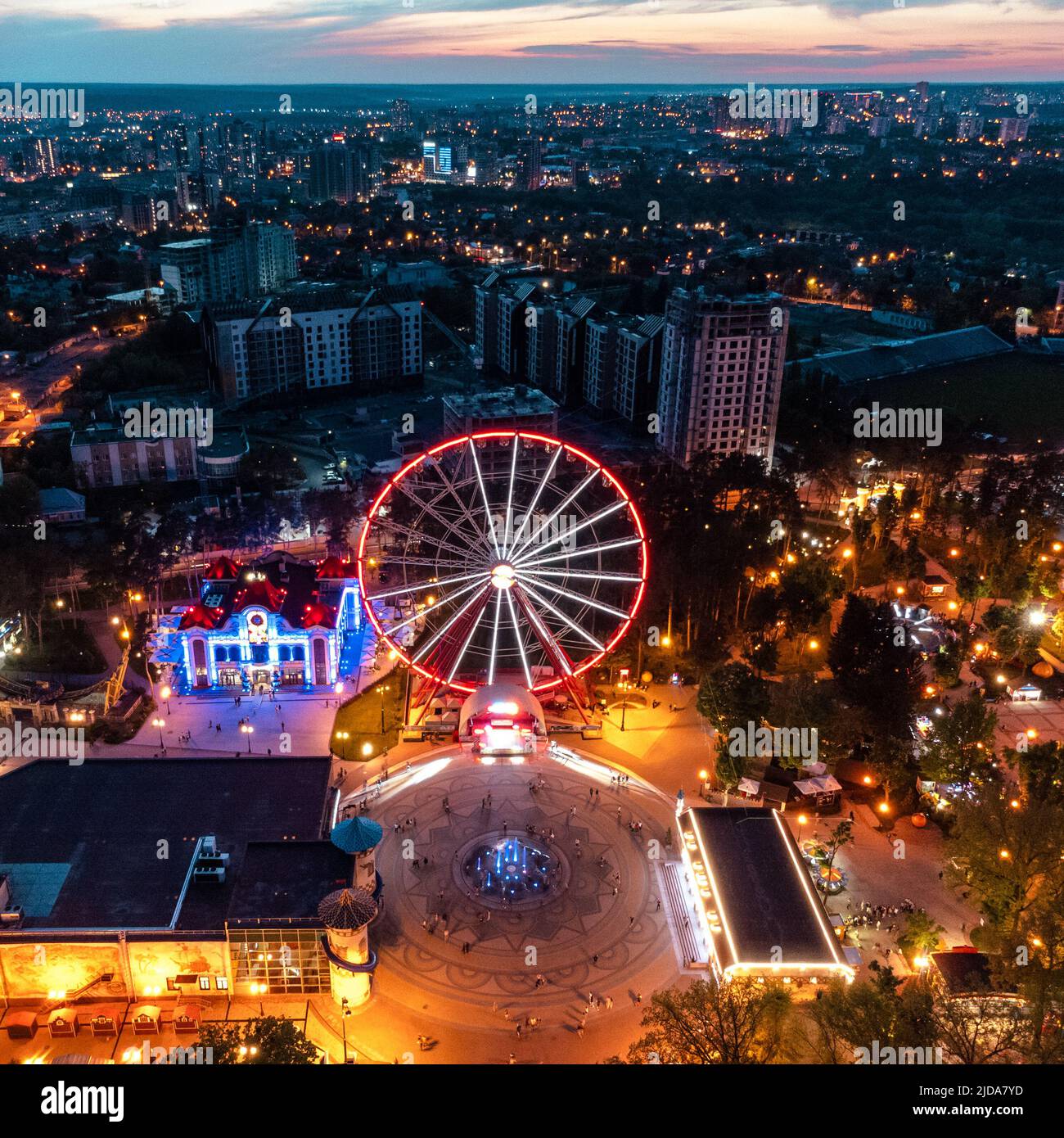 Ruota panoramica illuminata aerea e altre attrazioni. Zona ricreativa del centro di Kharkiv con luci serali. Divertimento Gorky Central Park al tramonto Foto Stock