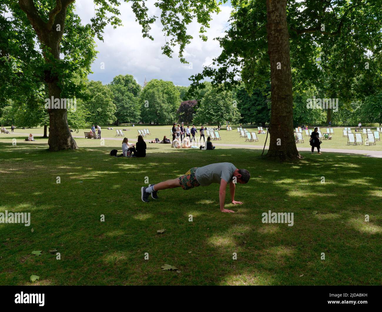 Londra, Greater London, Inghilterra, giugno 08 2022: L'uomo che si esercita in Green Park mentre la gente si rilassa dietro e le sedie a sdraio sono sparse intorno al parco. Foto Stock