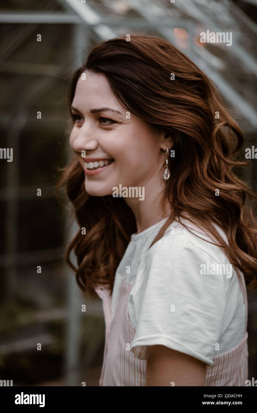 Bella donna al suo 30s nel giardino sera scuro. Bella donna ricci da sogno in serata camminando in abito lungo sopra serra. Moda Foto Stock