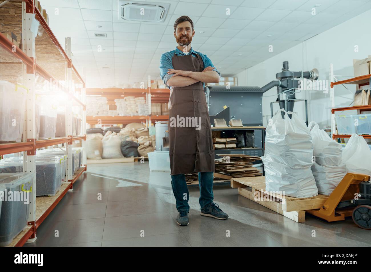 Il proprietario di affari sorridente sta in piedi sullo sfondo della macchina di tostatura del caffè Foto Stock
