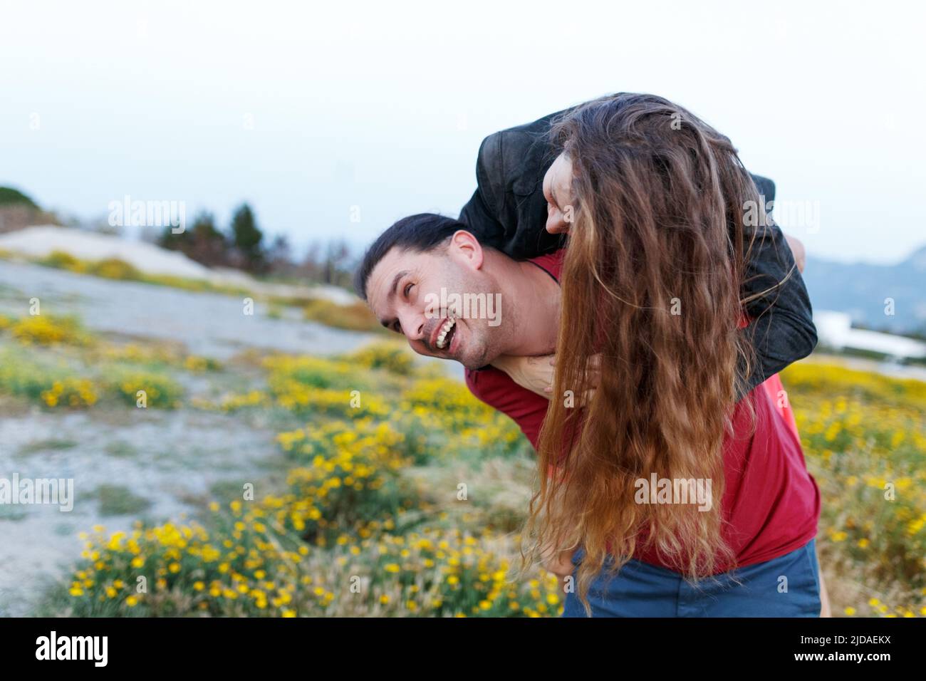Colpo di donna di mezza età che è trasportato dal suo ragazzo in campo d'erba. Coppia che si diverte durante la loro vacanza estiva. Foto Stock