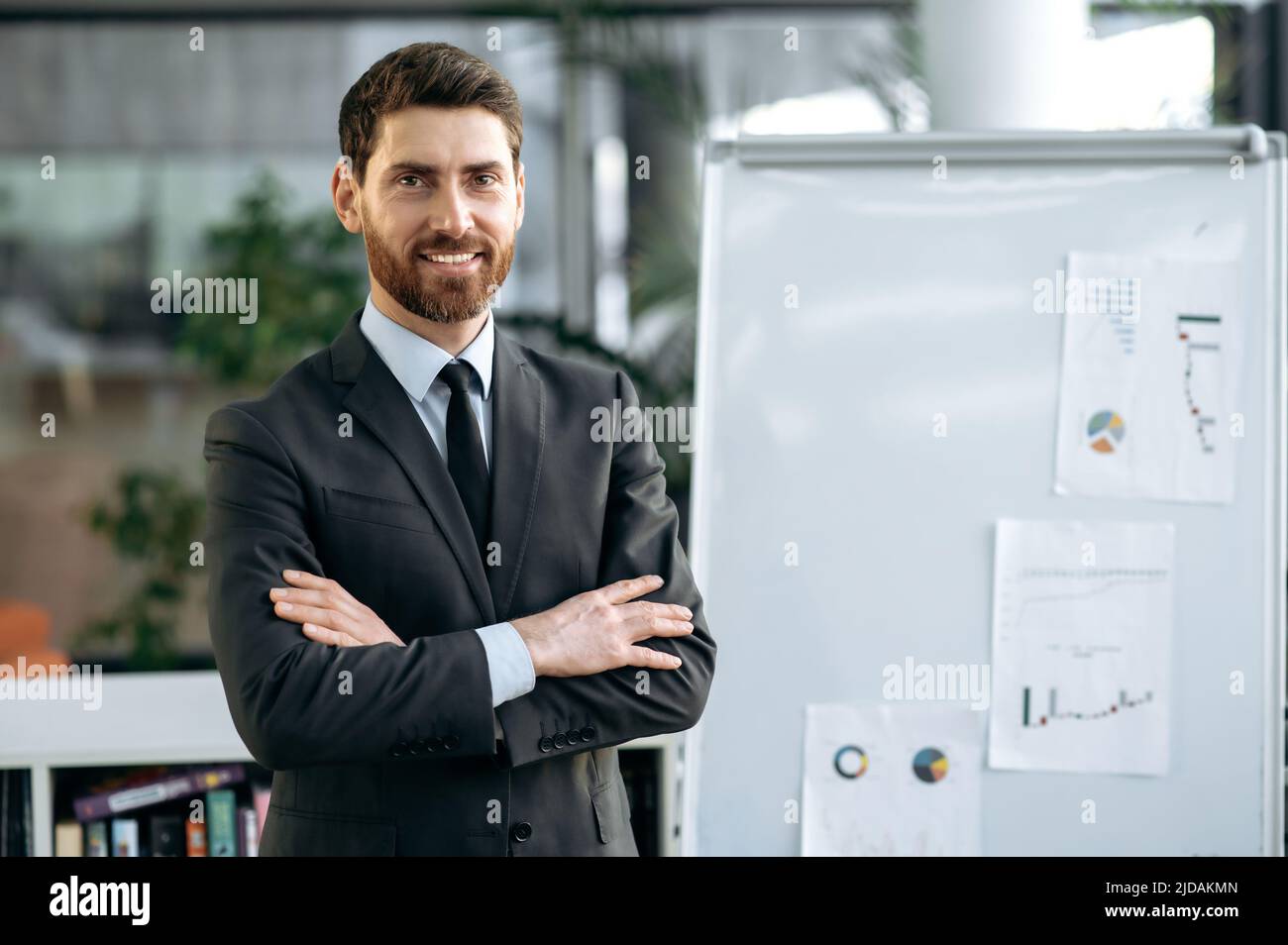 Rispettato intelligente caucasico maschio imprenditore, broker di borsa, si trova vicino a lavagna bianca con grafici in ufficio moderno, indossare abbigliamento business, braccia incrociate, guardando la macchina fotografica, sorridente amichevole Foto Stock